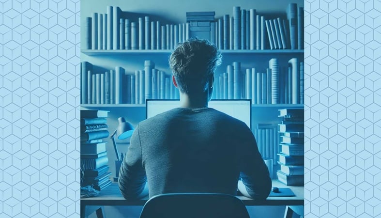 A man at the computer in front of a bookshelf, from behind